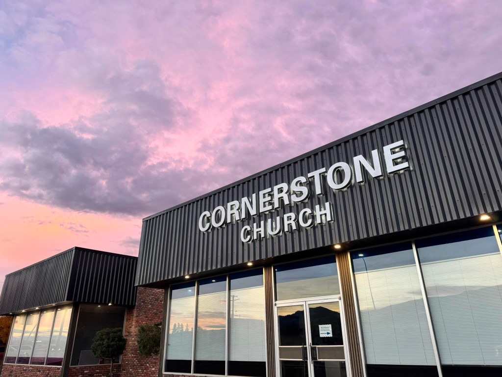 The front of the Cornerstone Church building at dusk, with the church name lit above the entrance and a pink and purple sky overhead