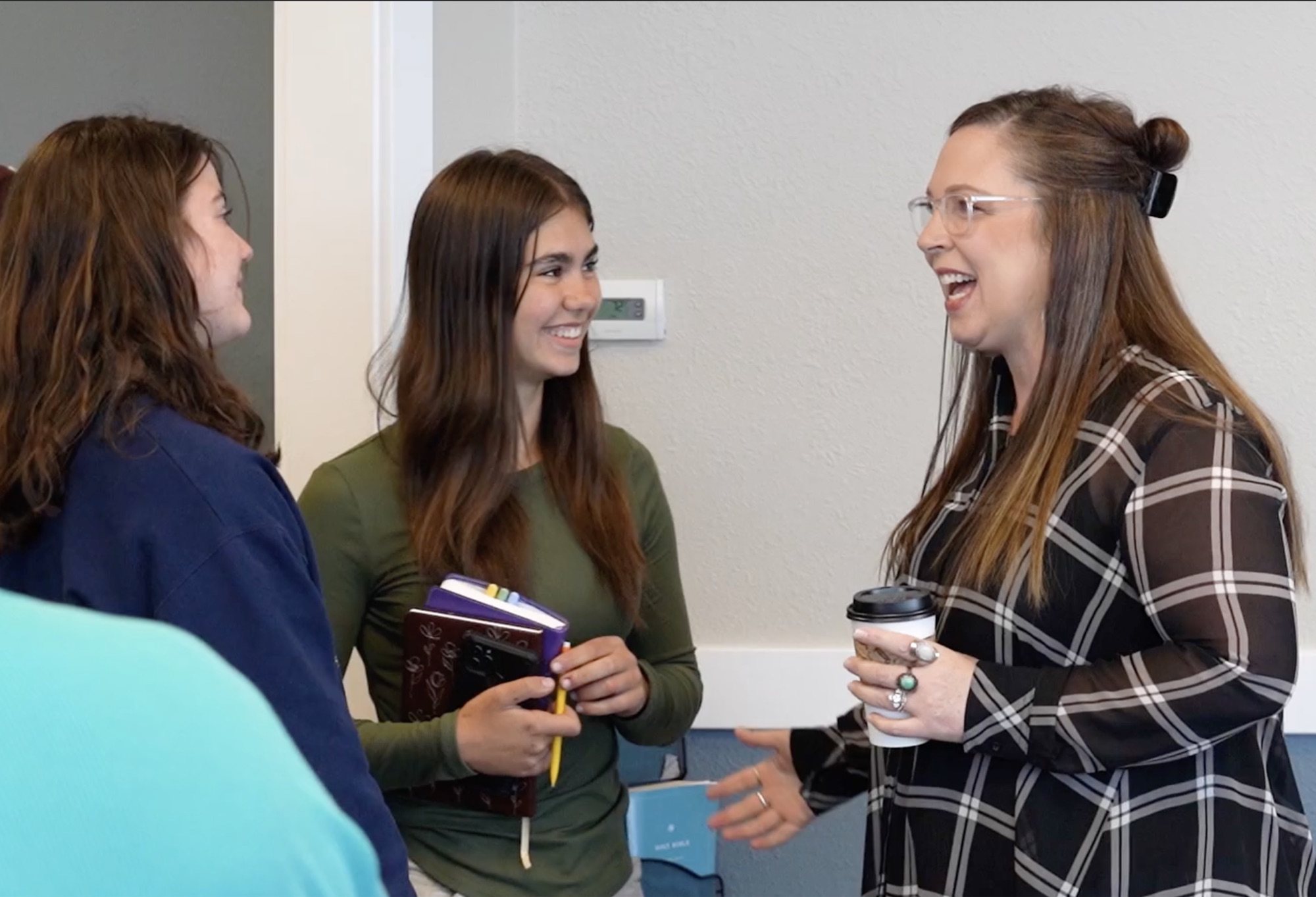 Three women laughing together with coffee and Bibles in hand
