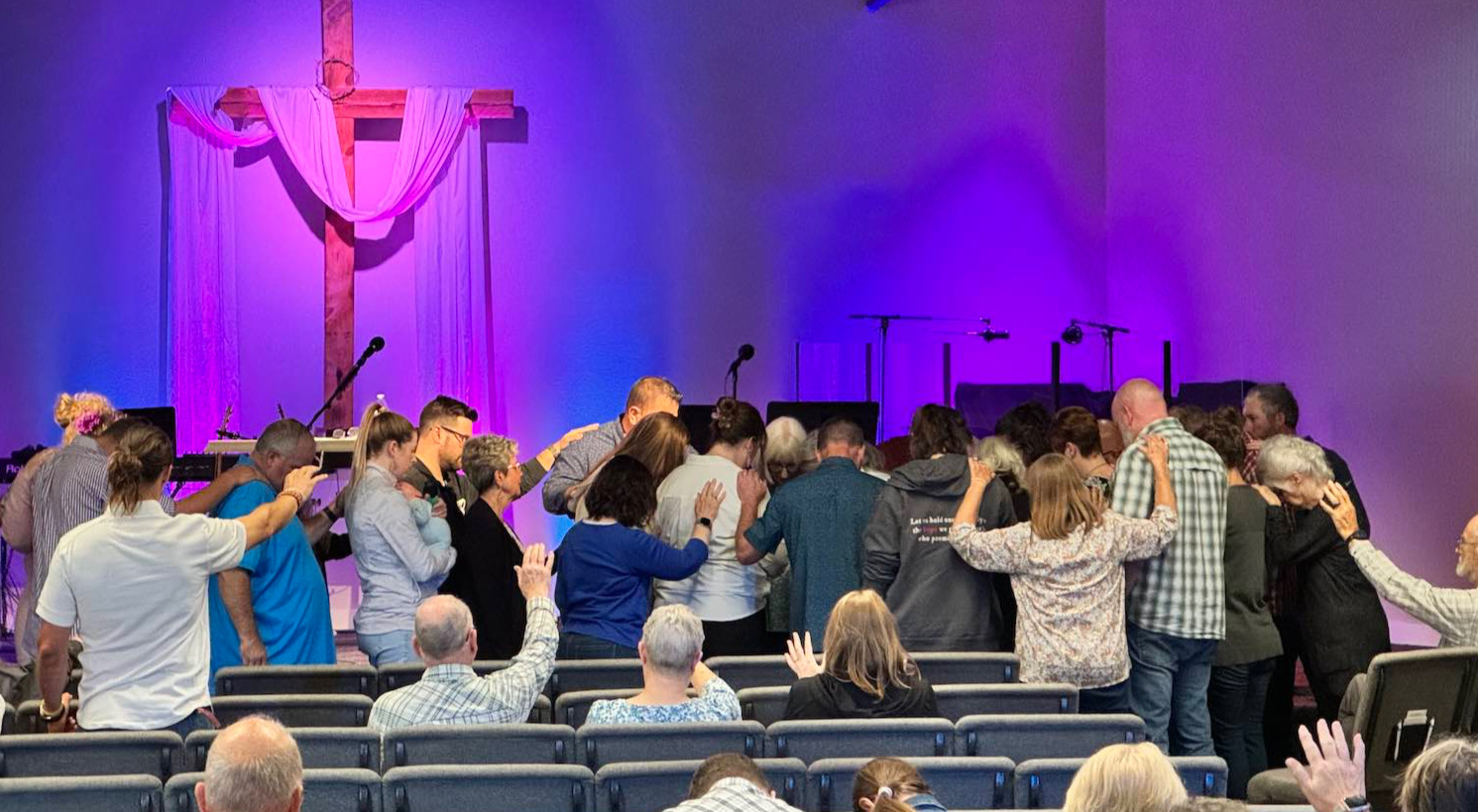 The congregation gathered at the front of the sanctuary, praying together with hands on one another's shoulders