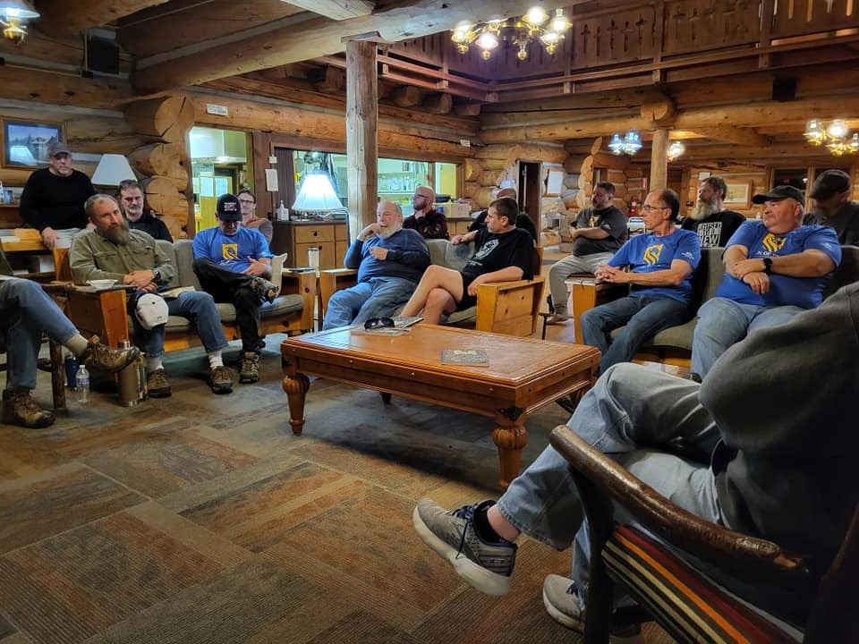 Men of Cornerstone sitting together in a log lodge during their yearly retreat