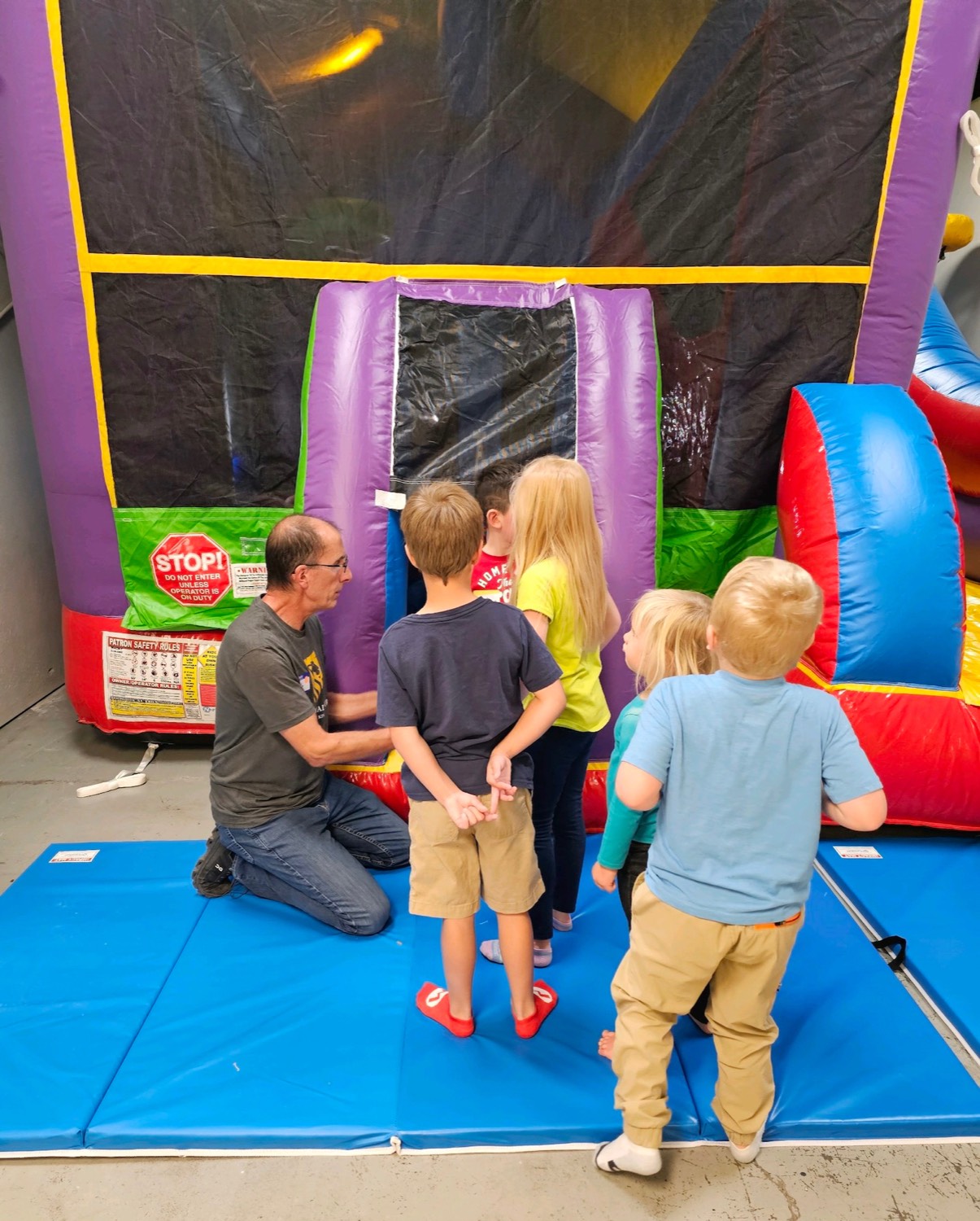 A volunteer kneeling beside a bounce house, talking with children at Parents Night Out